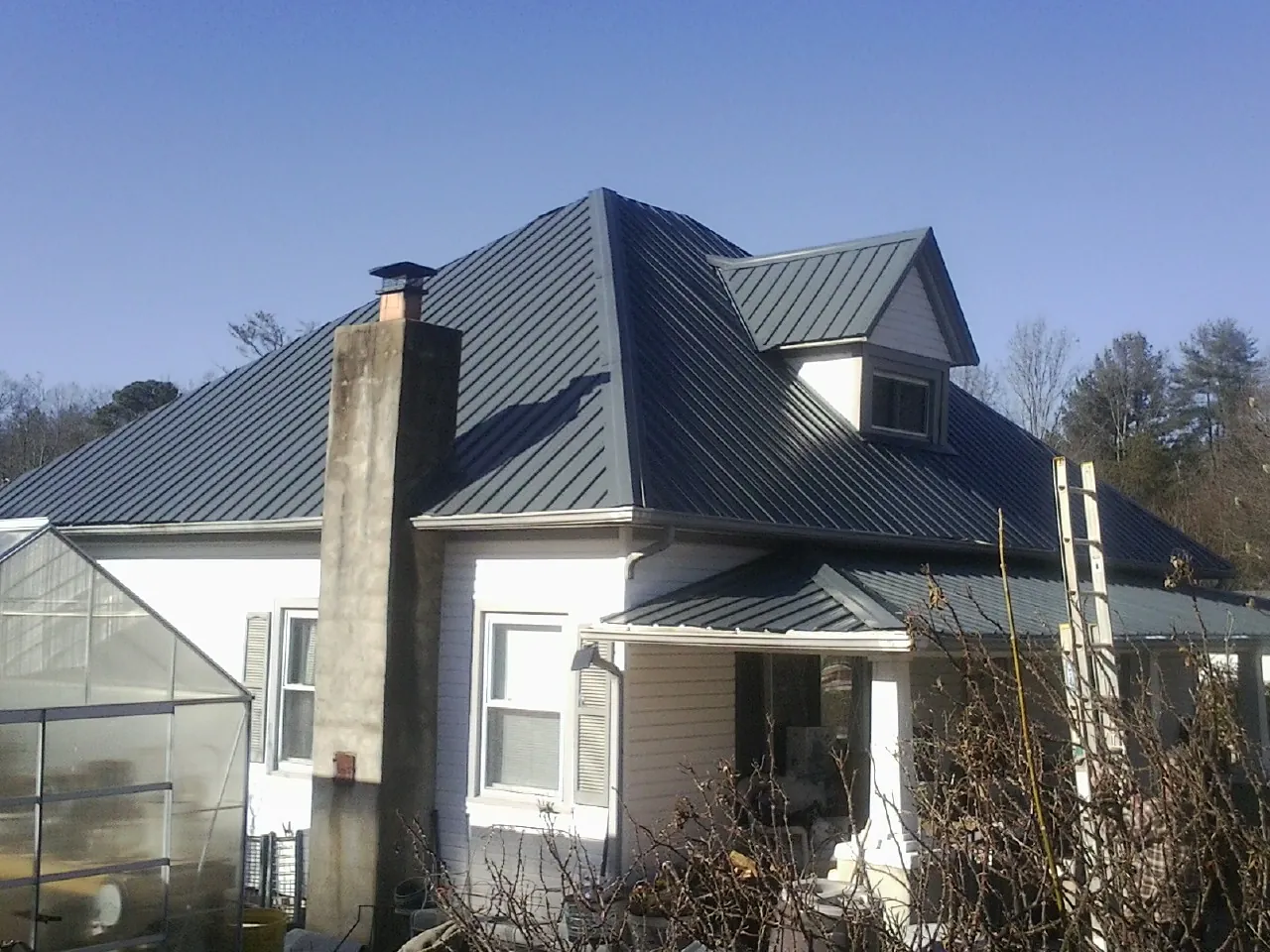 Dark blue standing seam metal roof on a white farmhouse with dormer — Slate & Tile Roof Repair by Roofing Brothers in West Liberty
