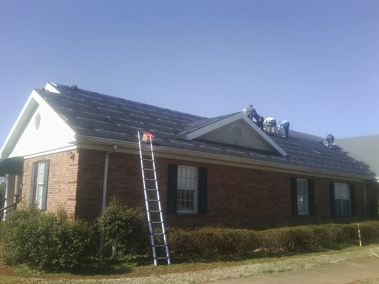 Crew tearing shingles off a brick ranch roof with a ladder set — Emergency Roof Repair work by our crew in West Liberty