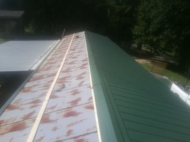 Old rusted panels beside newly installed green metal roofing — Wind Damage Roof Repair by Roofing Brothers in West Liberty