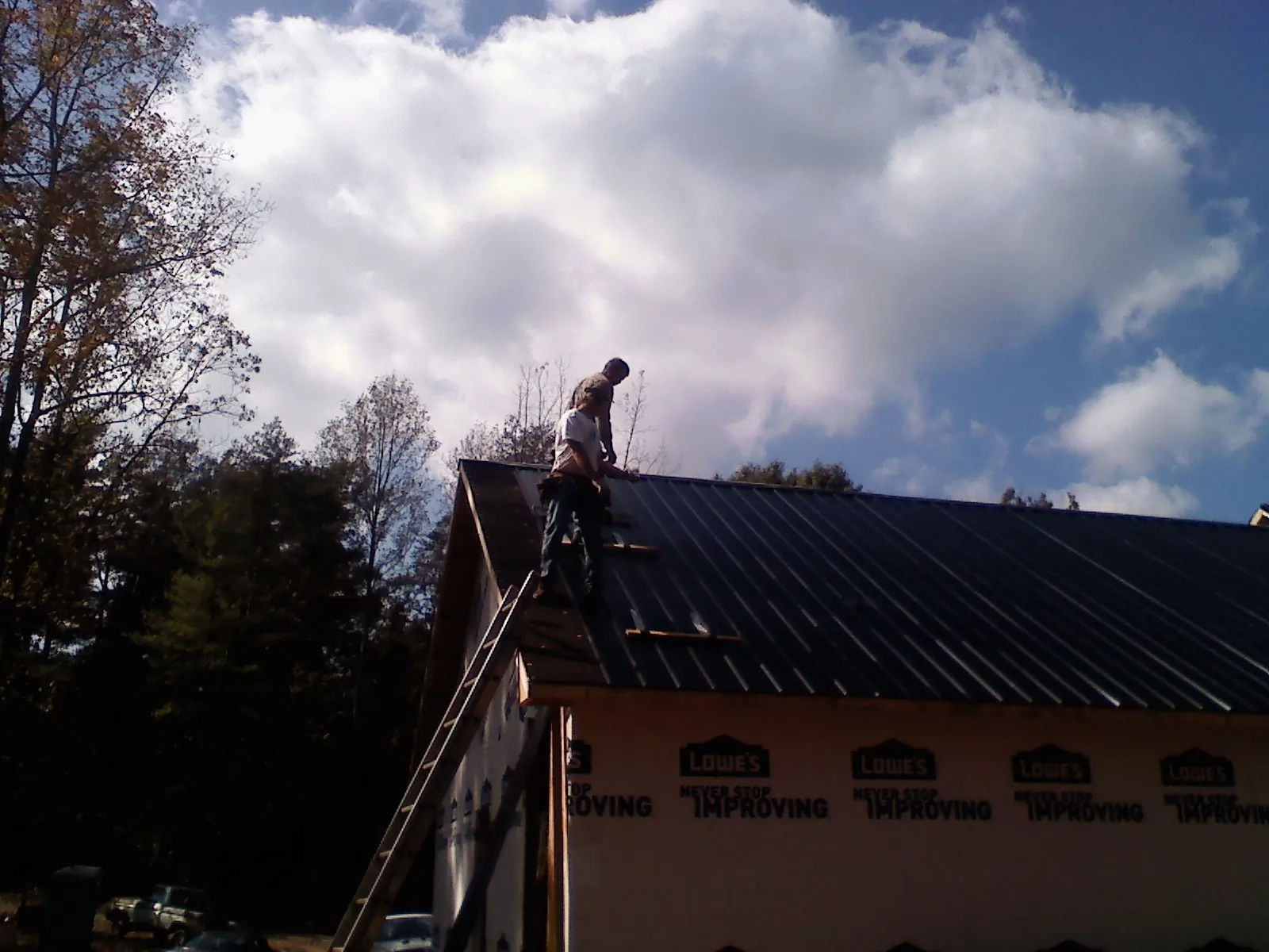 Roofer fastening dark metal panels high against a cloudy sky, from a Roof Inspection job in West Liberty