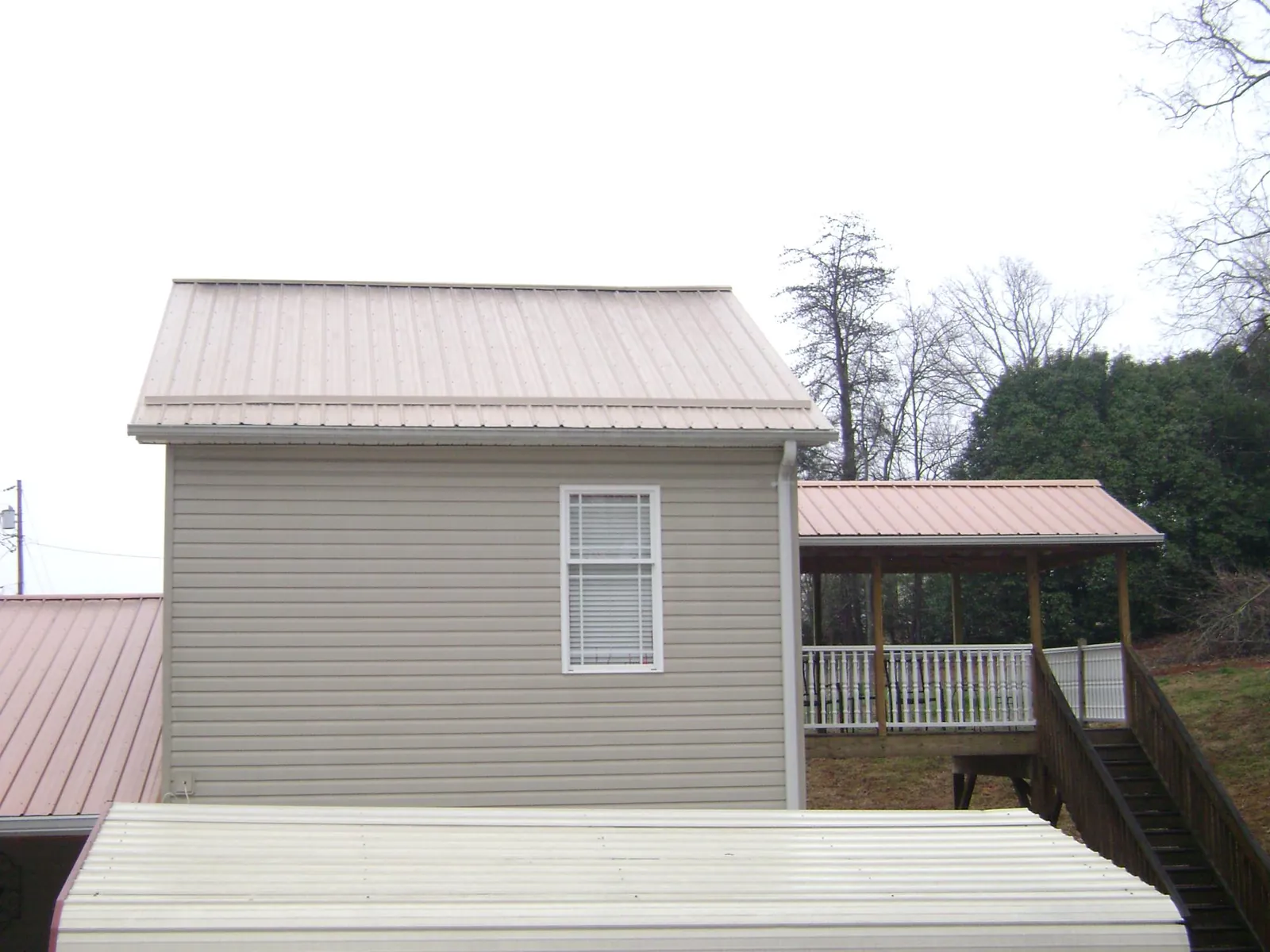 Tan metal roofs on a two story addition and attached porch, from a Roof Replacement job in West Liberty